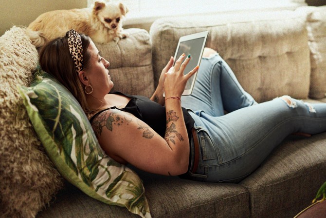 Woman laying on couch with dog and tablet