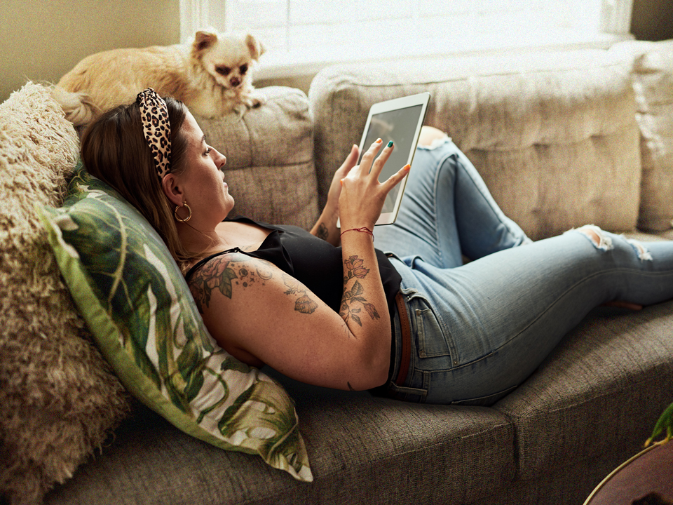 Woman laying on couch with dog and tablet