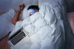 A person lying in bed sleeping with a laptop on their bed