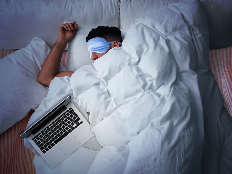 A person lying in bed sleeping with a laptop on their bed